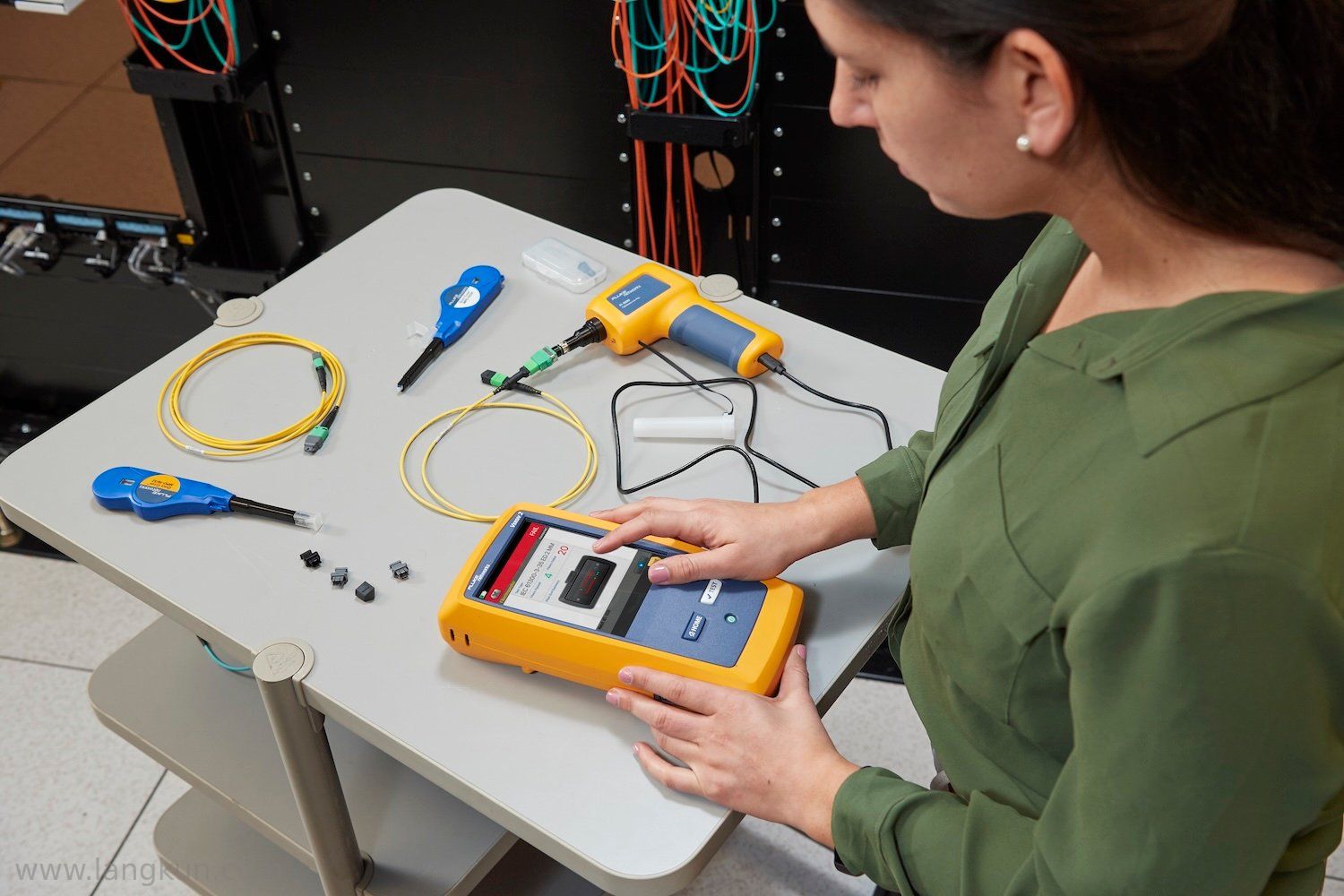 一位穿绿色衬衫的女士使用FI-3000 FiberInspector Pro检查一条刚清洁过的光纤电缆,该电缆放置在灰色桌面上